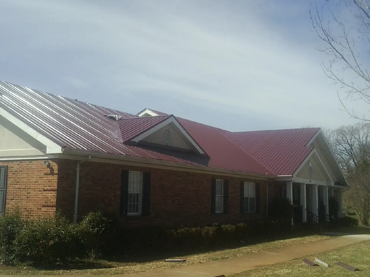 Red metal roof with gabled entries on a long brick building, from a Hail Damage Roof Repair job in Masontown